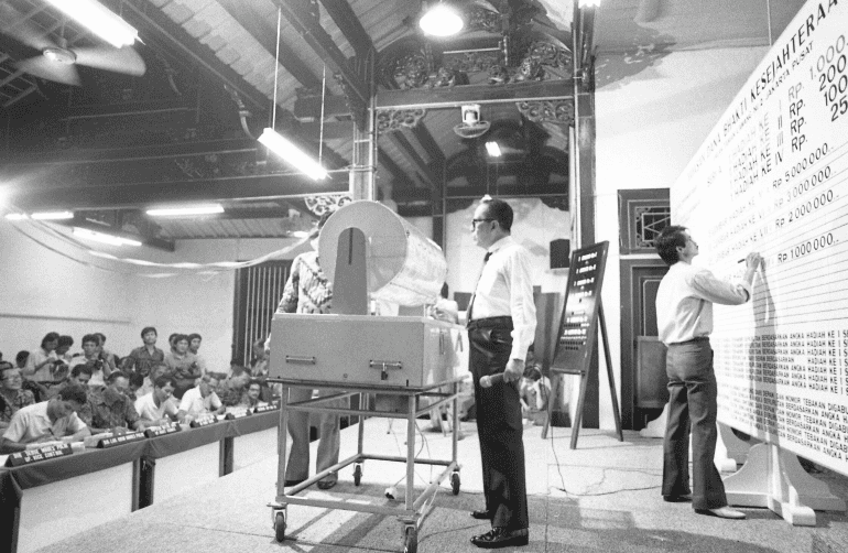 Dokumentasi kegiatan pengundian resmi berhadiah di Indonesia pada era Orde Baru, menampilkan proses pencatatan hasil undian di hadapan peserta dan aparat.
